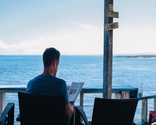 A relaxed man reading a book on a sunny balcony overlooking the sea