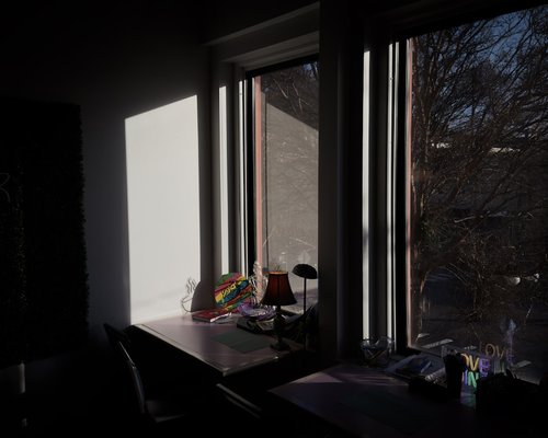 A neat desk set up with a laptop and a cup of water, sun streaming in through the window
